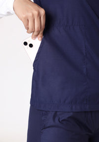 Close-up of a smartphone being placed in the Knya scrub top's pocket.